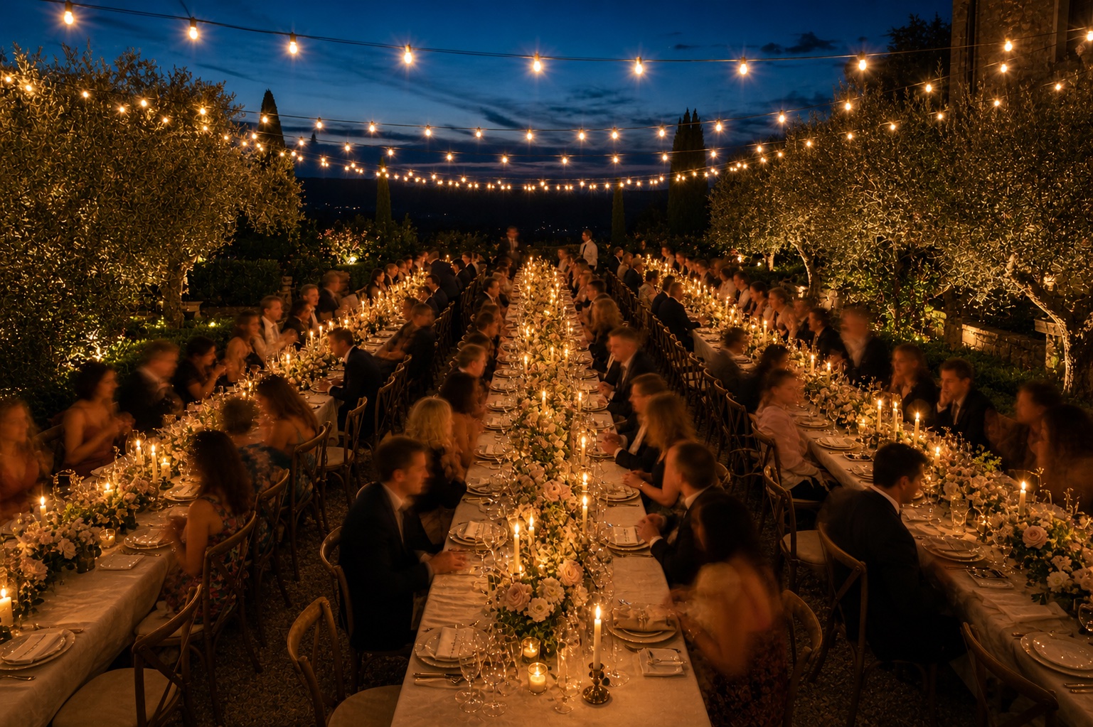 Long candlelit banquet tables under string lights at a Tuscan estate wedding at blue hour