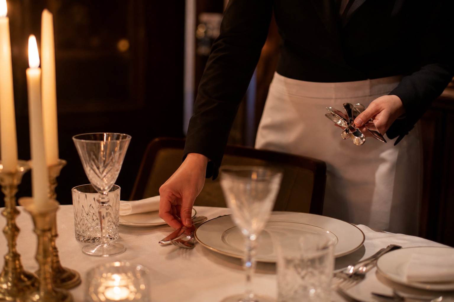 Server in crisp uniform setting an elegant table by candlelight